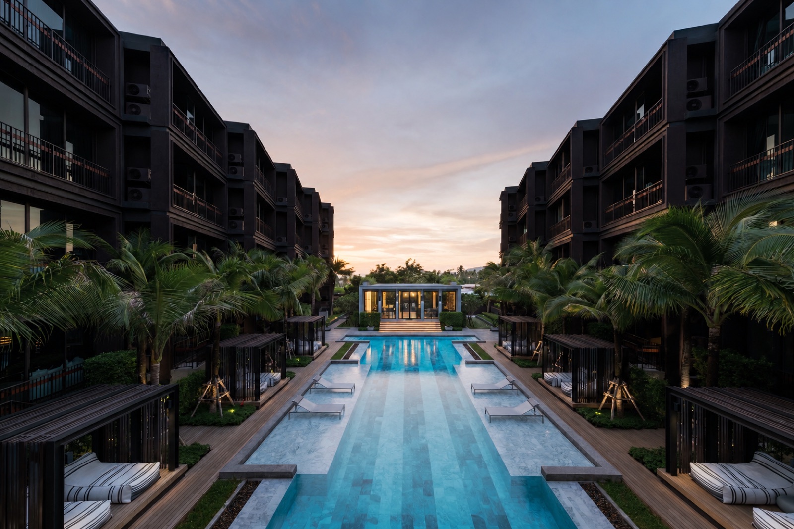 Resort pool lined with cabanas and palms at sunset